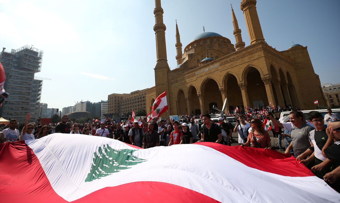 Manifestantes carregam bandeiras nacionais durante um protesto contra o governo no centro de Beirute, Líbano, em 20 de outubro de 2019