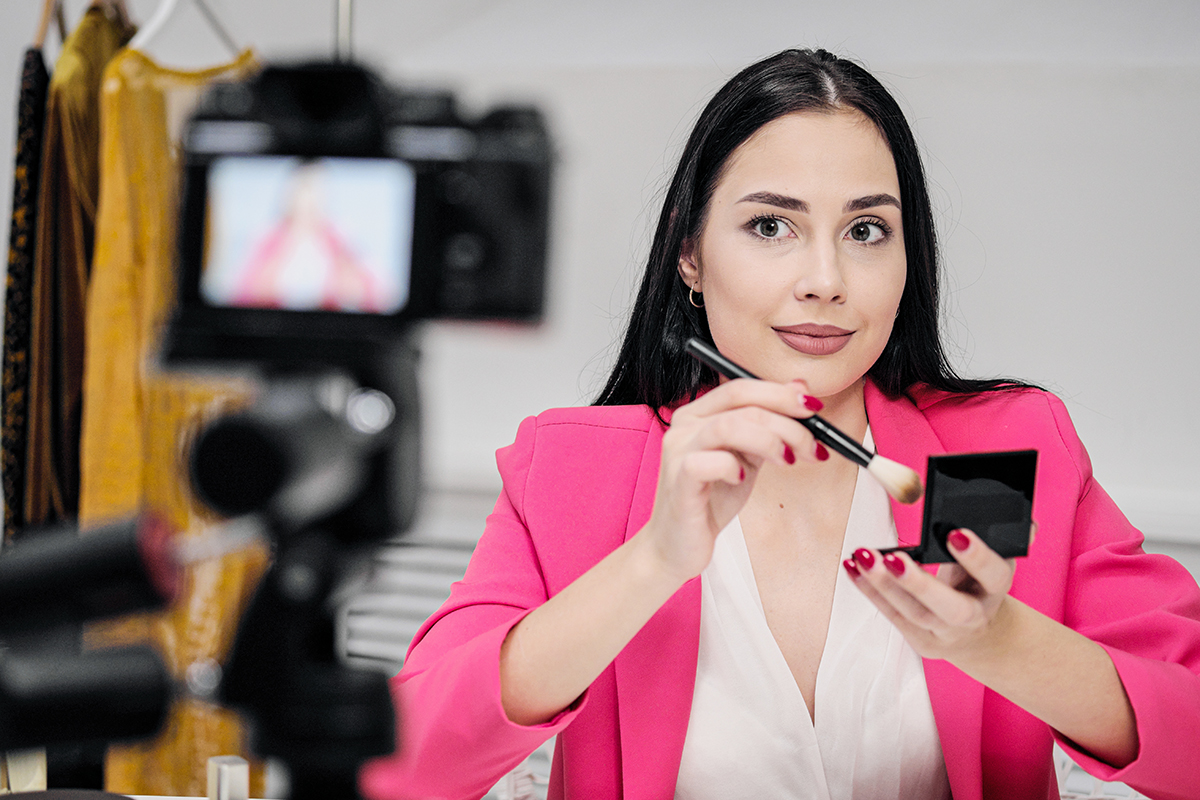 A beautiful young woman blogger in a pink jacket shoots a blog about cosmetics. The concept of vlog and freelancing.