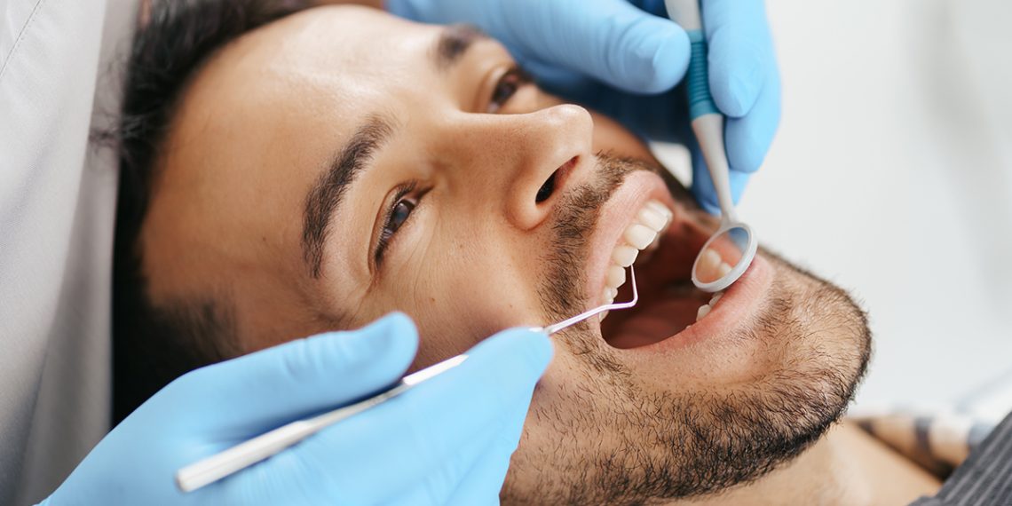 Smiling,Young,Man,Sitting,In,Dentist,Chair,While,Doctor,Examining