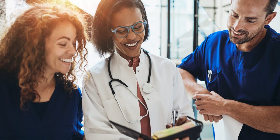Smiling group of diverse doctors discussing a patient's dignosis while standing together in a hospital corridor