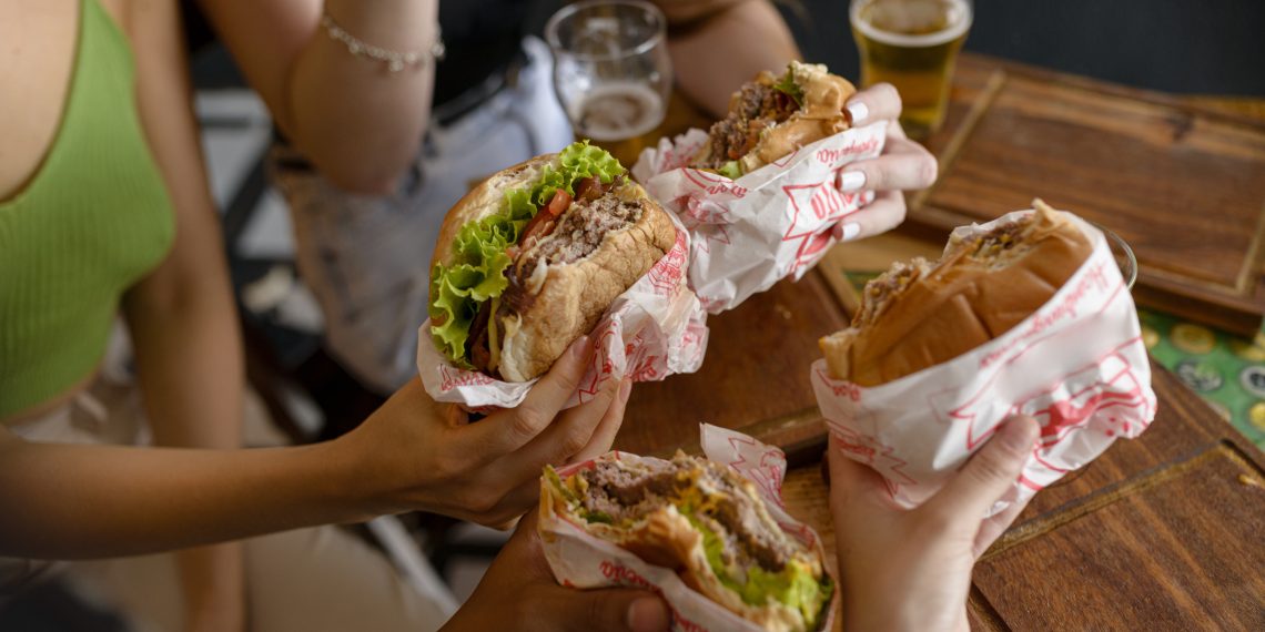 Detail of snacks in hands of groups of young people in pub.