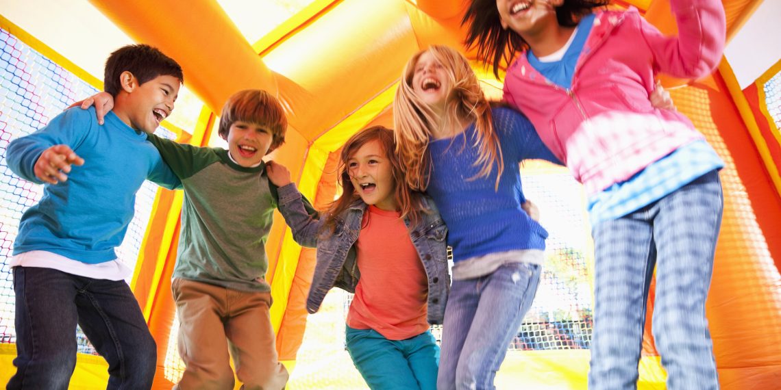 Multi-ethnic group of excited children (ages 7 to 10 years) jumping in inflatable bouncy castle.