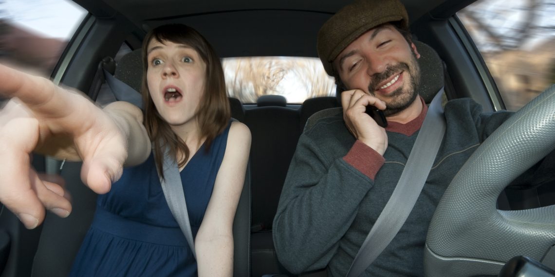 A young woman sees an accident coming, while the man, who is driving, is talking in his cell phone (Motion blur that demonstrates movement)