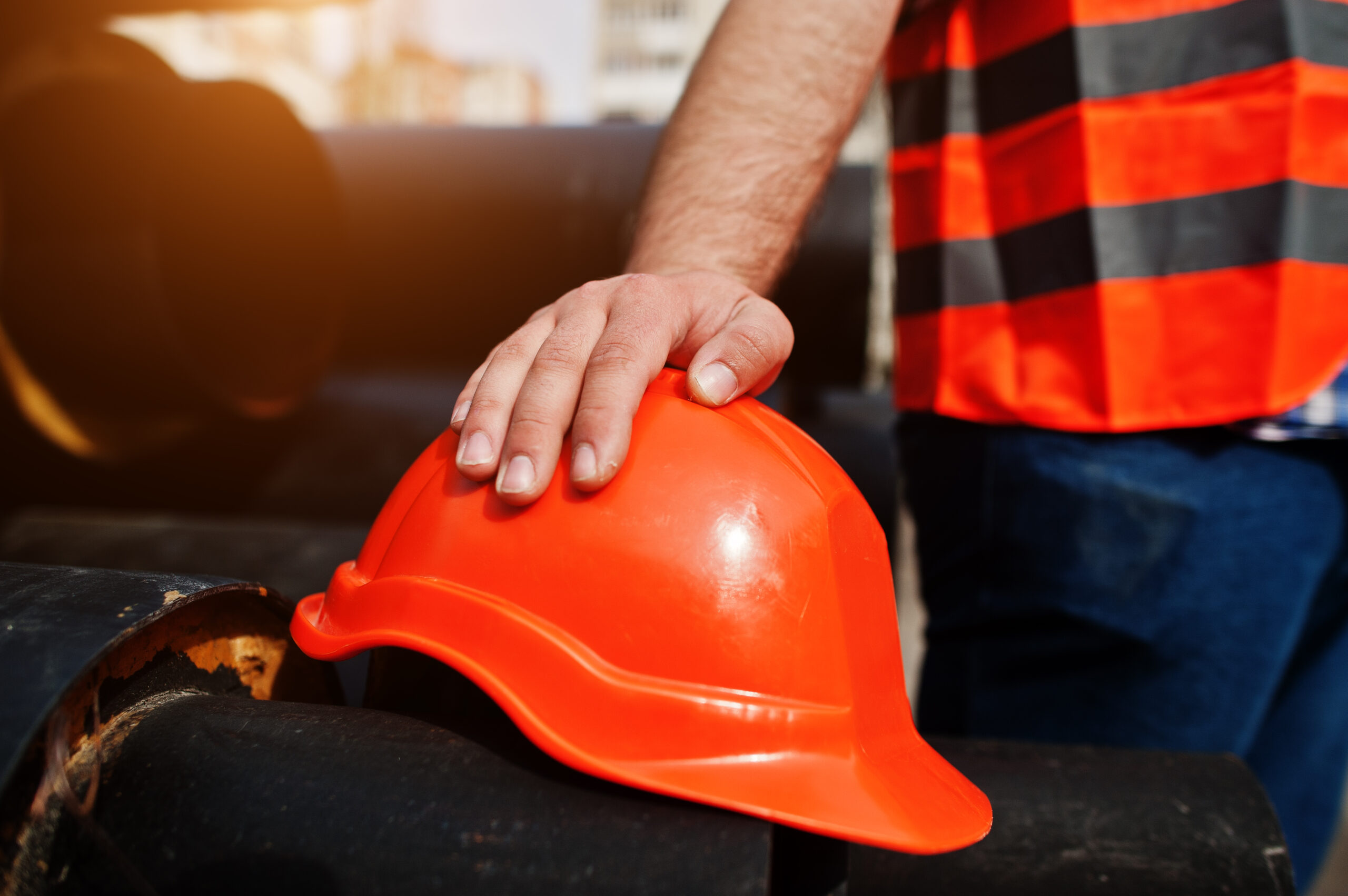 Hand of worker man in safety orange helmet near steel pipes.