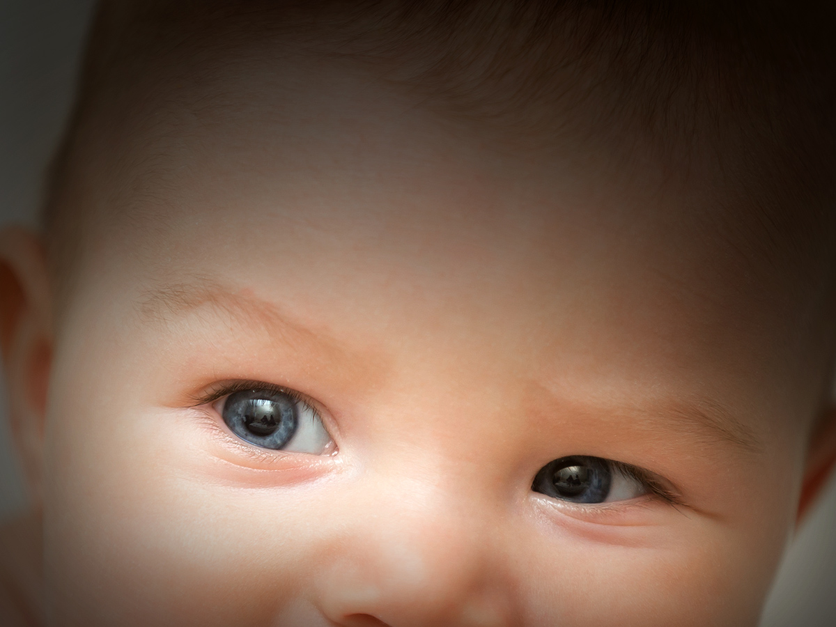 Adorable baby smiling and biting the board of his wooden cot, teething process. Family, home concept photo, close up