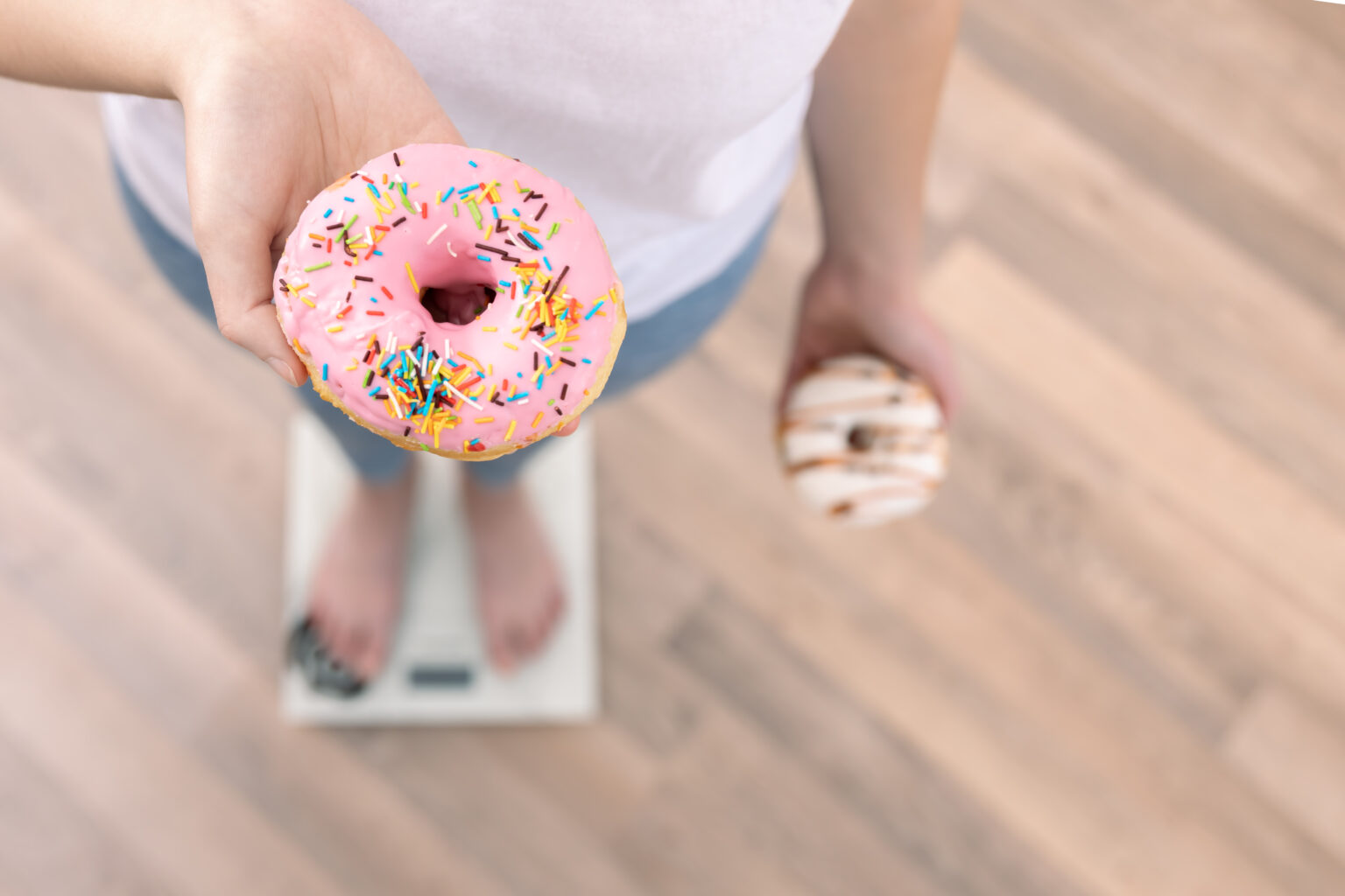 A woman stands on the scales, holds donuts in her hands, the concept of diet, weight gain, weight loss, proper nutrition, sweet.